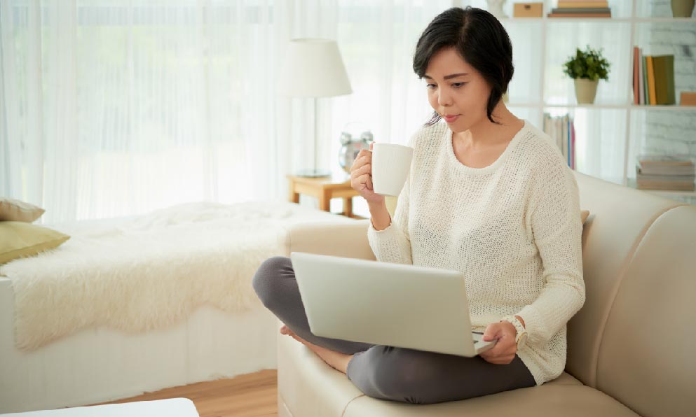 穿白色長袖灰色褲子拿著咖啡看著電腦影片的女生