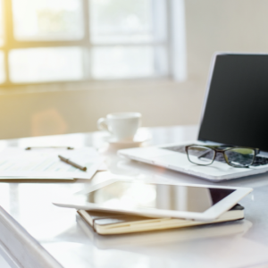 桌上有一台筆電，筆電上有眼鏡。桌上有輸有平板有紙筆有咖啡