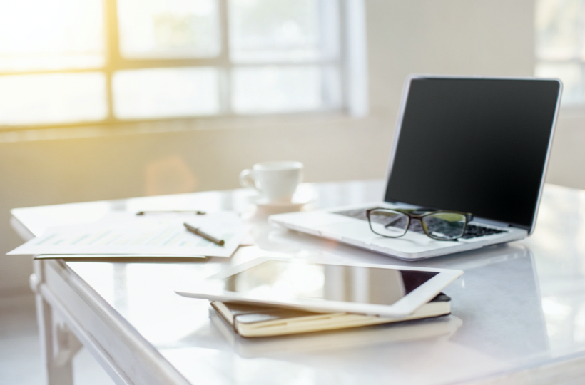 桌上有一台筆電，筆電上有眼鏡。桌上有輸有平板有紙筆有咖啡