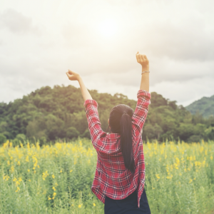 一個穿紅格子襯衫的綁馬尾女生在草原中高舉雙手
