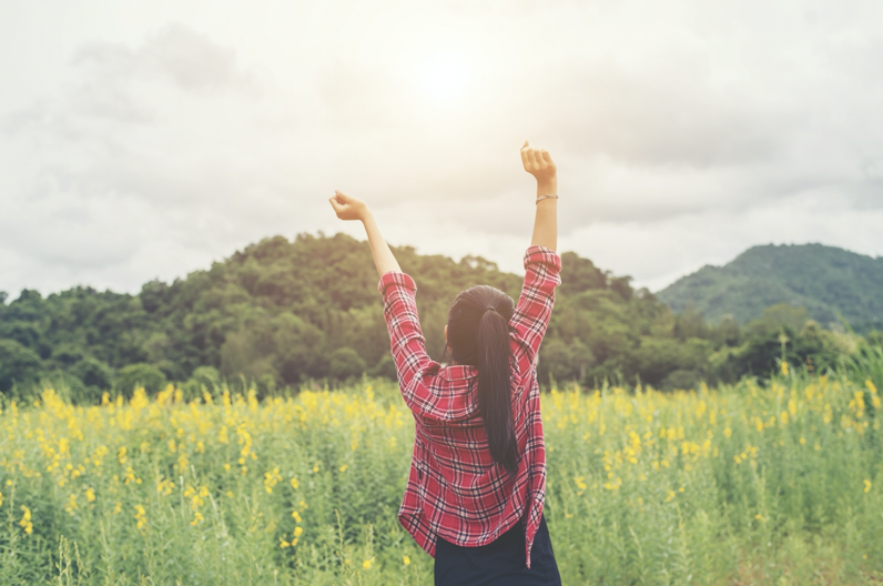 一個穿紅格子襯衫的綁馬尾女生在草原中高舉雙手